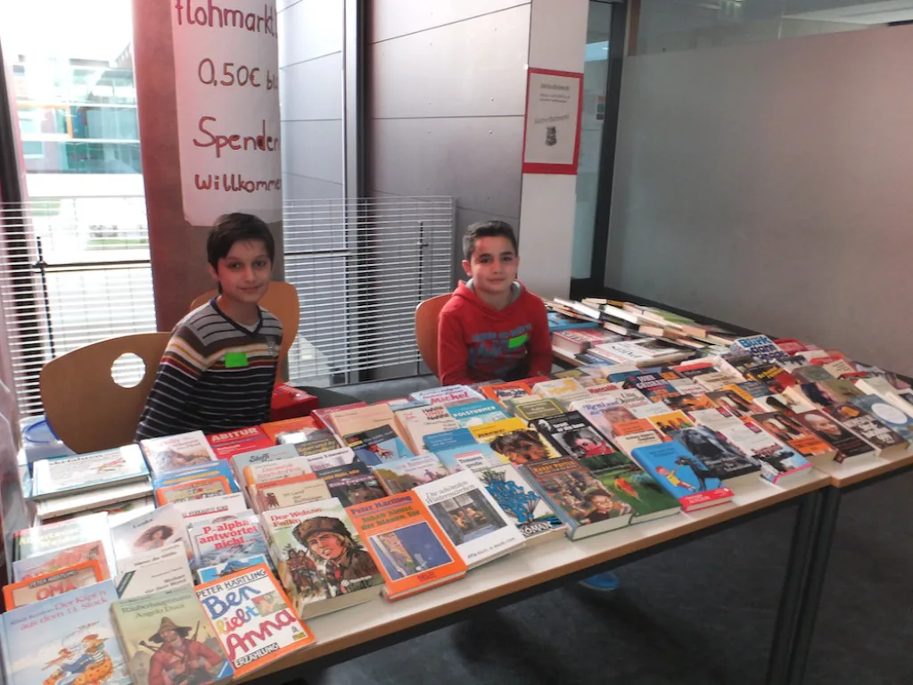 Kinder sitzen hinter einem Tisch mit Büchern des Flohmarkts.
